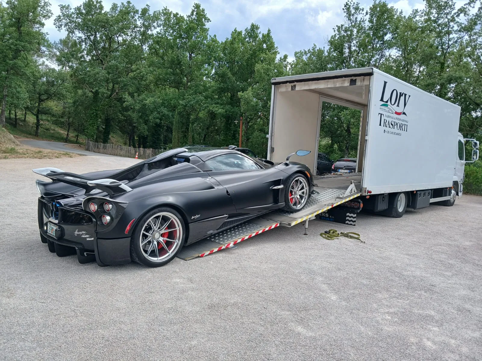Black sports car just off the ramp of the closed Lory Trasporti van, tailgate open